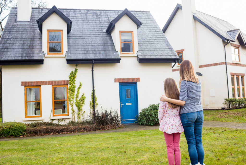 A blond woman and blond girl are looking at a small doghouse cape home, possibly deciding if they would like to live there. A Crow's Nest Inspection can help them decide. Hudson Valley Capital Region NY Home Inspection.
